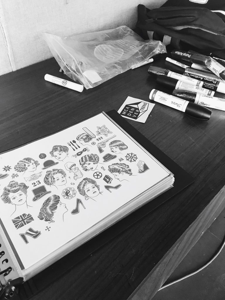 A sketchbook is opened on a table filled with depictions of traditional america tattoo designs