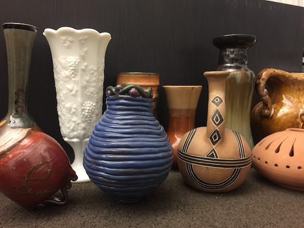 Several works of pottery against a dark backdrop. They vary in color and design but are all small sized vessels. 