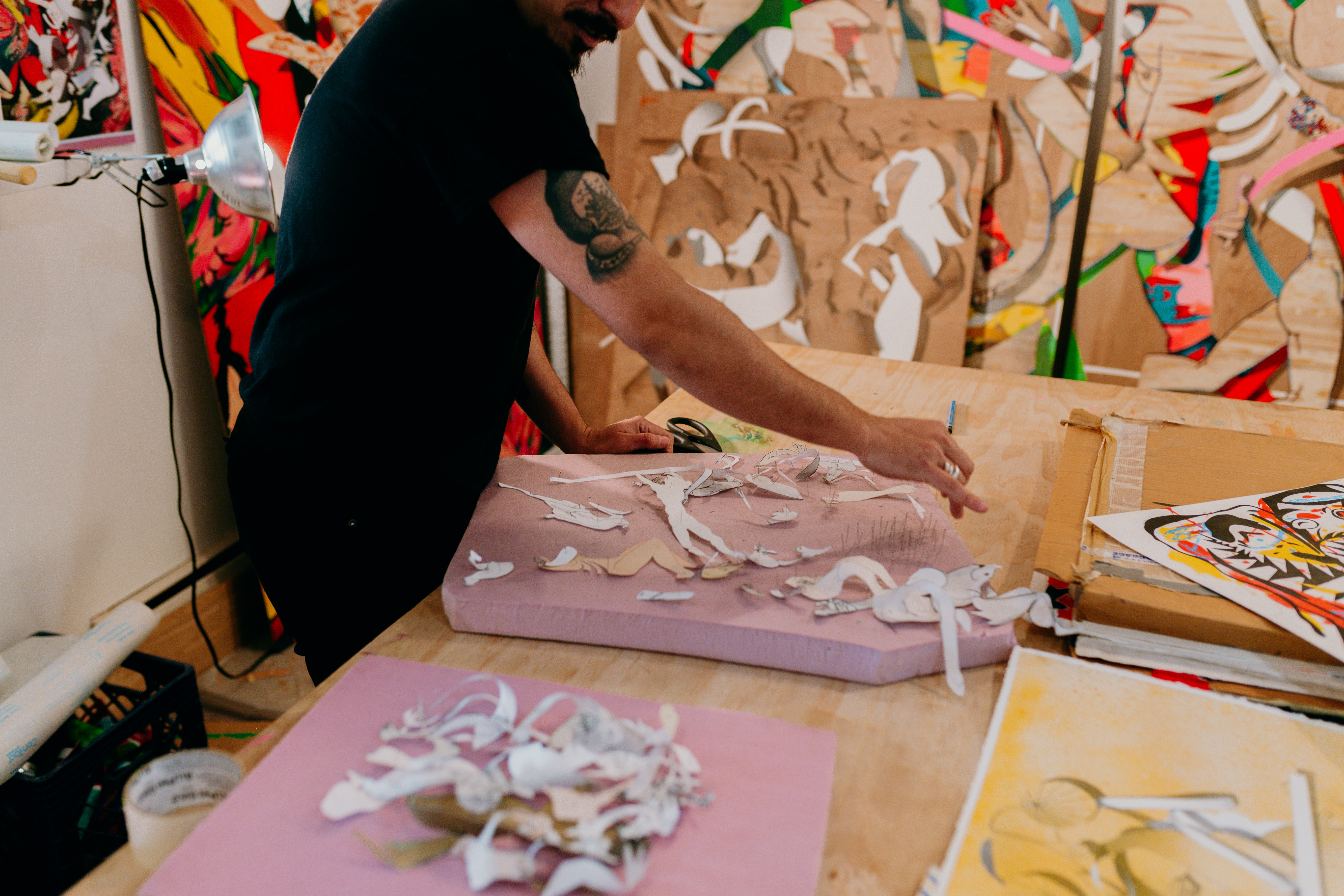 Candid shot of a man working in a studio surrounded by wood panel artworks and styrofoam .