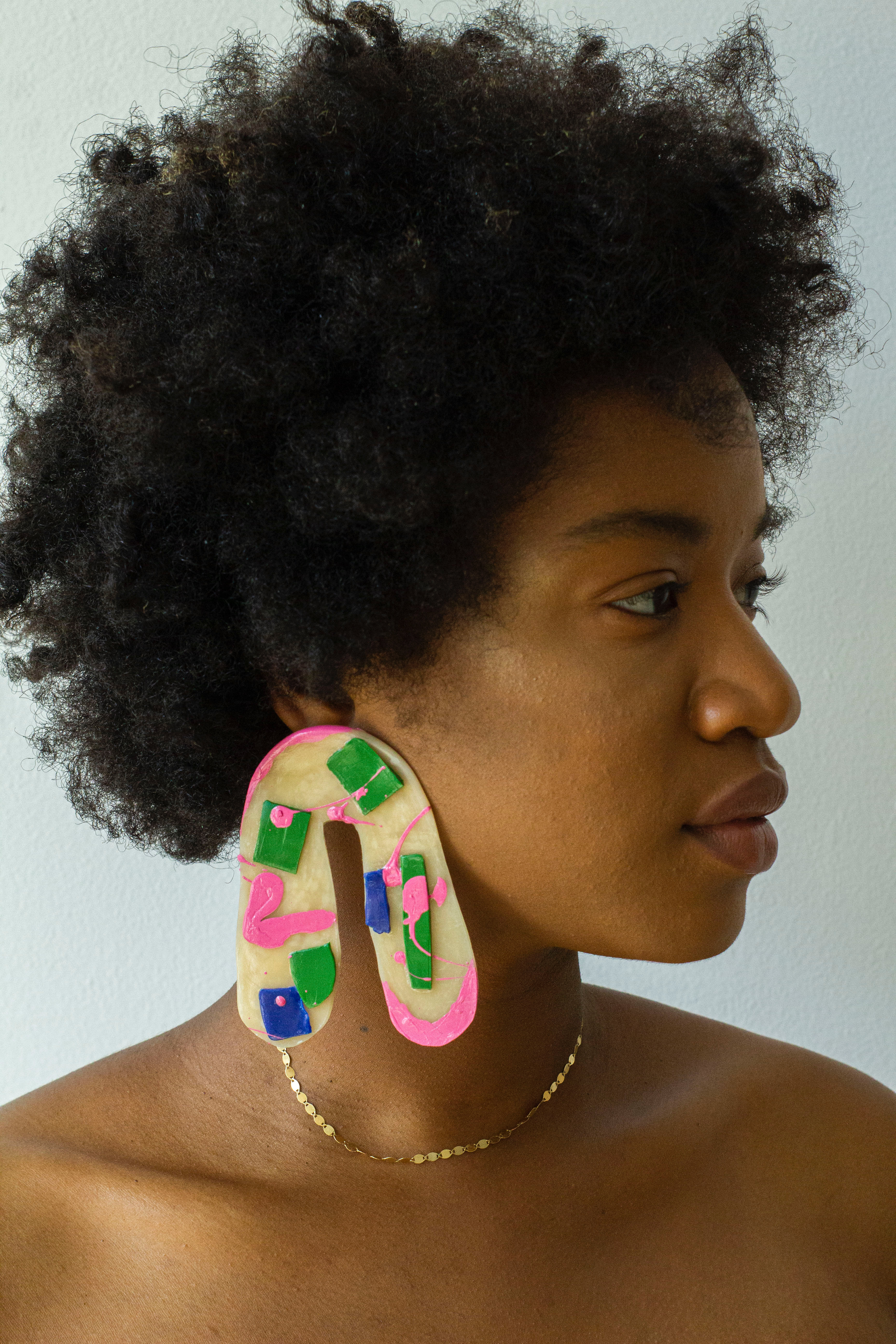 Close up portrait of Jaylan Rose, wearing big arch shaped earrings that are beige, pink, blue, and green.