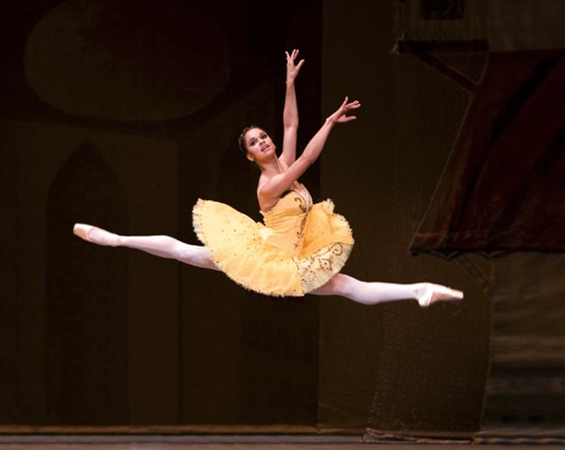 Misty Copeland in a yellow ballet tutu, in midst jump, arms elongated 