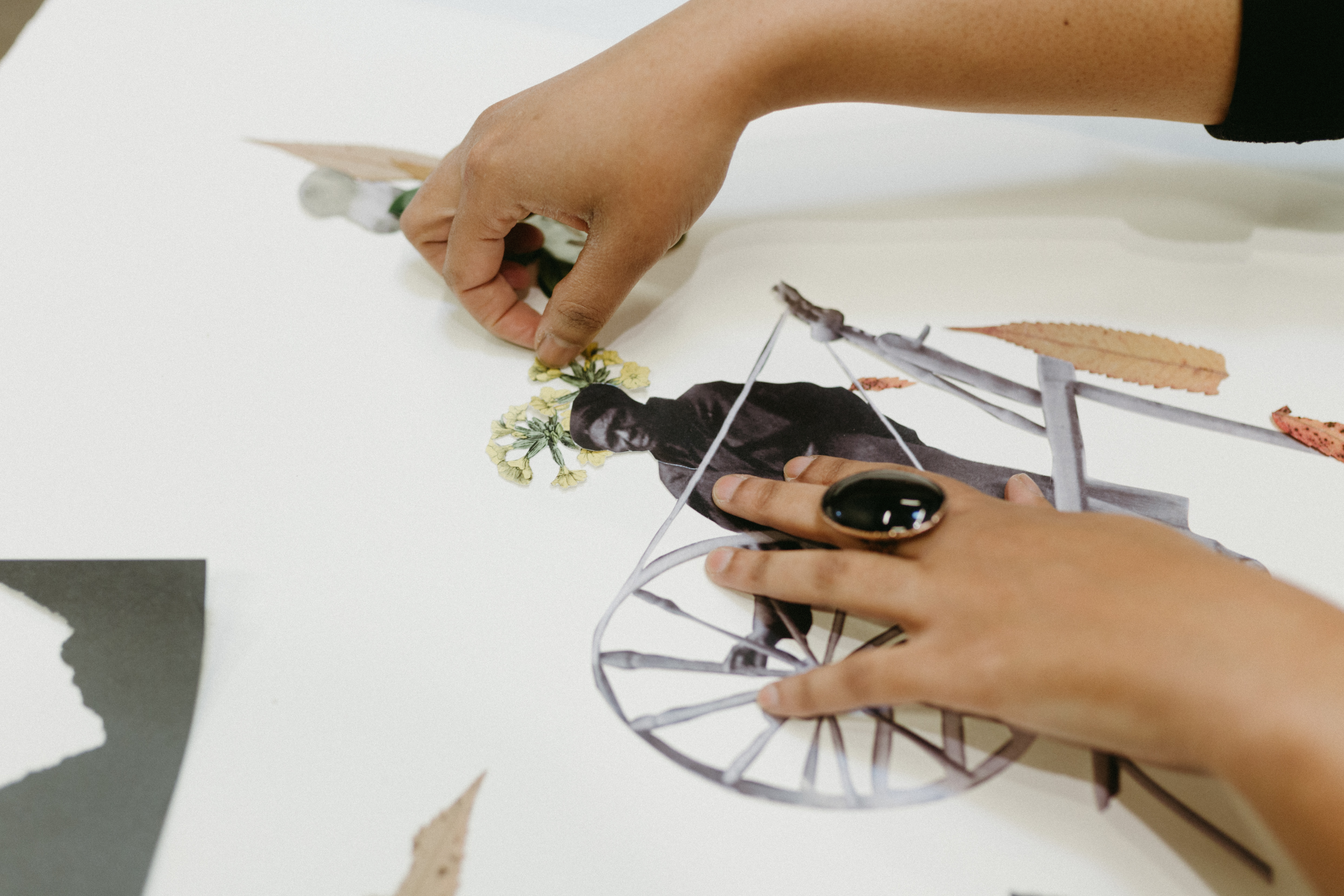 Close up image of Anthony's in-process collage work. She is placing cut out image of yellow flowers on a woman's head who is working on a spindle. 