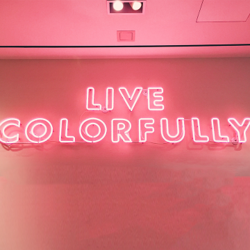 Pink neon light is hung upon a wall indoors reading Live Colorfully
