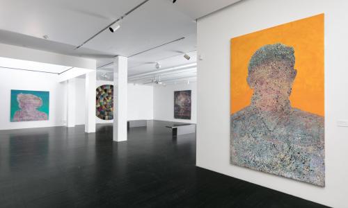 A gallery space filled with large paintings hanging on white walls. The artworks are abstract depictions of unidentifiable people. Almost like a silhouette. 