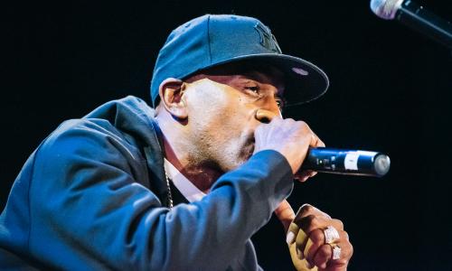 Photo of rapper Rakim rapping into the mic, with a ball cap and hoodie