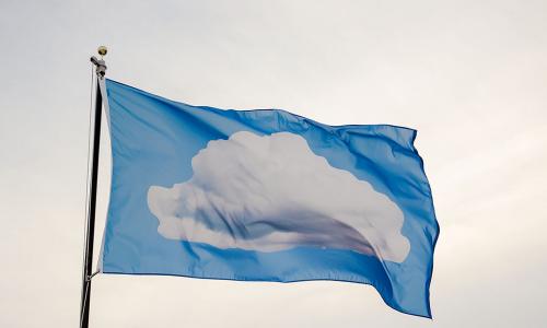 Sky blue flag against an overcast off white sky. The flag has a white cloud in the center.